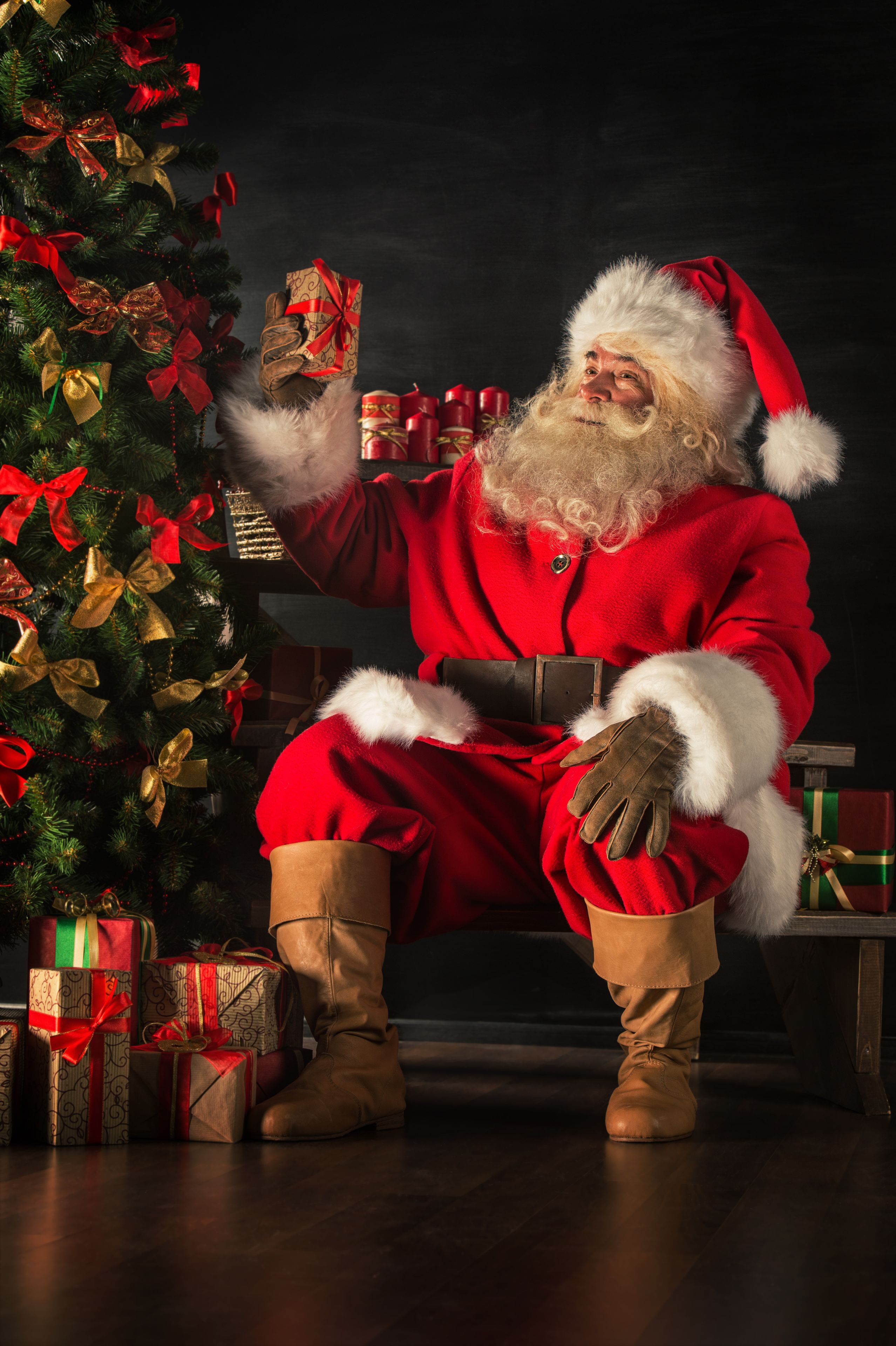 father christmas holding a resent next to a christmas tree