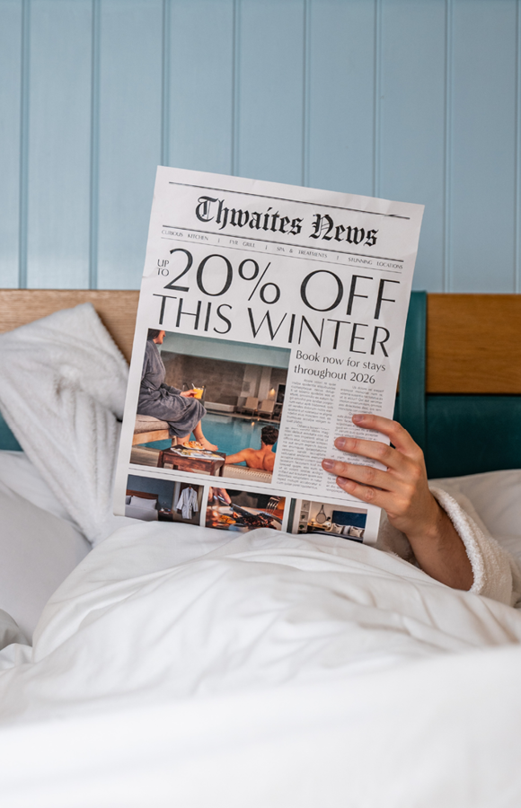 "up to 20% off this winter" newspaper being held in a hotel bed